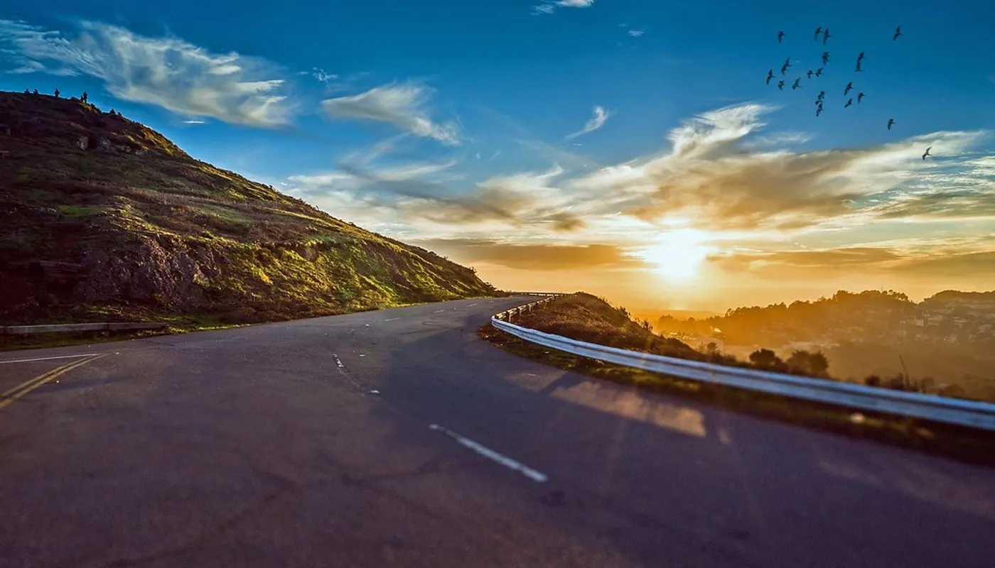 An empty road curving into a sunset over the hills